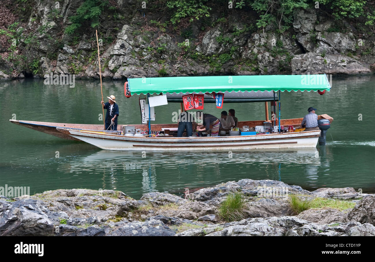 Ein Boot hält an, um Essen in einem schwimmenden Restaurant am Oi-Fluss in Arashiyama, außerhalb von Kyoto, Japan, zu kaufen, eine beliebte Wochenendbeschäftigung für Einheimische Stockfoto