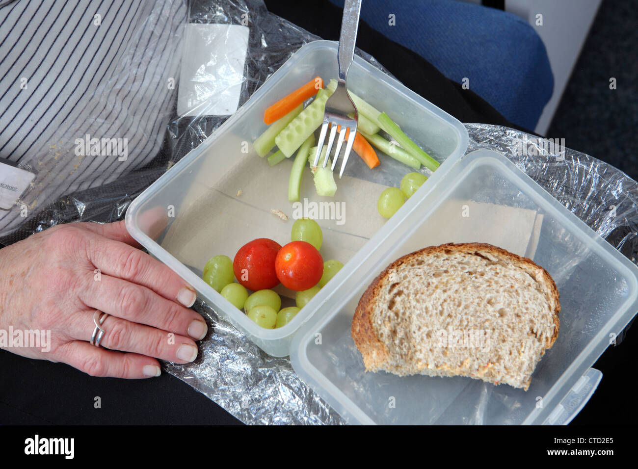 Nahaufnahme mit Hand. Gesunder Arbeitsplatz Essen günstig, verpackten Mittagessen auf Schoß, Salat in Kunststoff-Box, School, England, UK Stockfoto