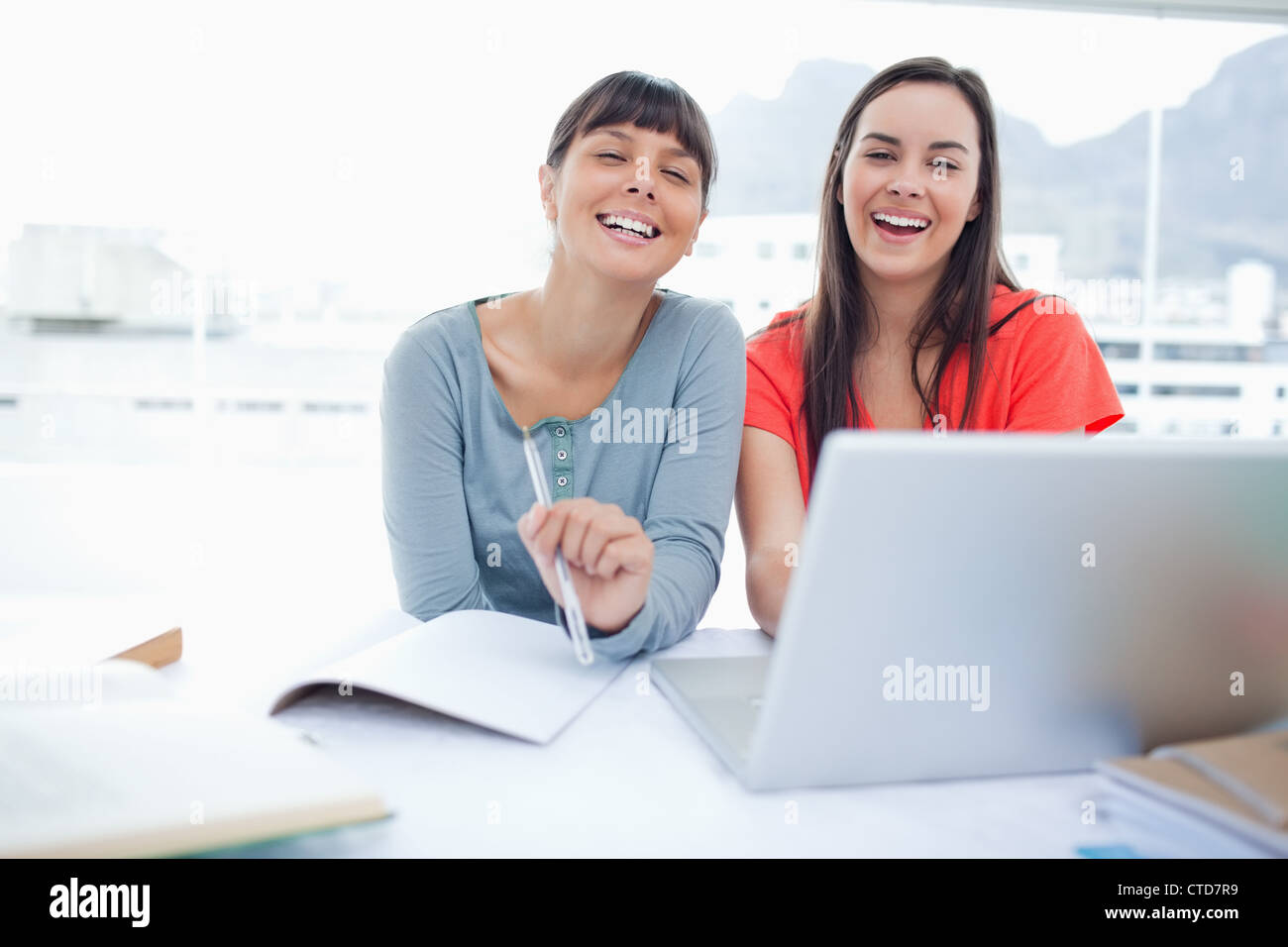 Zwei lachende Mädchen sitzt vor einem Laptop zusammen vor der Kamera Stockfoto