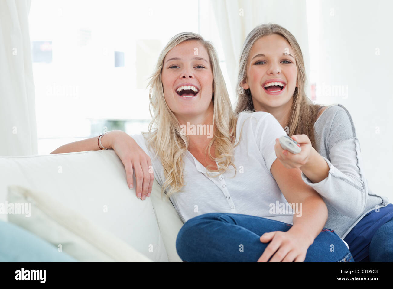 Lachende Schwestern sitzen auf der couch Stockfoto