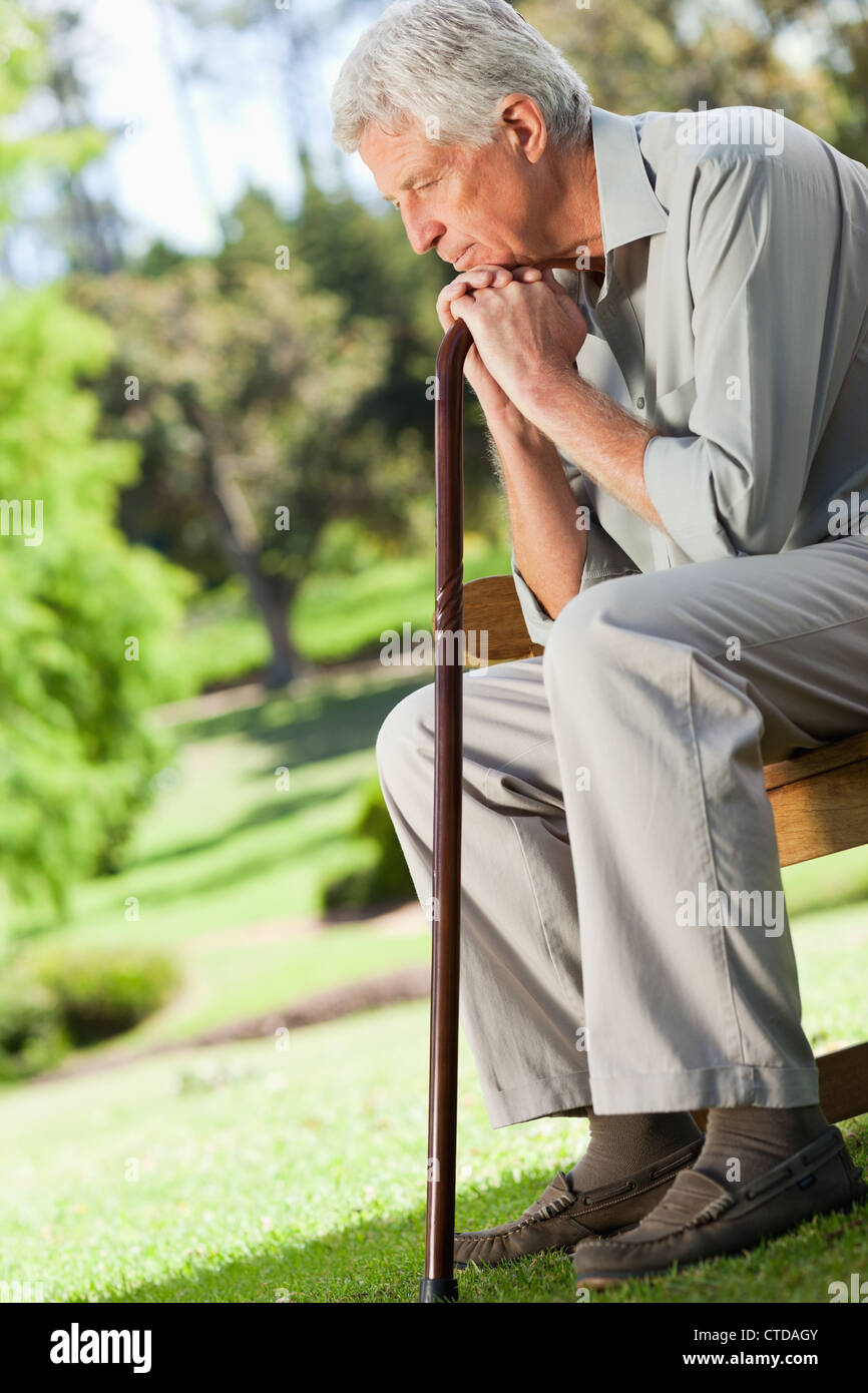 Alter Mann sitzen ruht seine Hände auf seinen Spazierstock Stockfoto