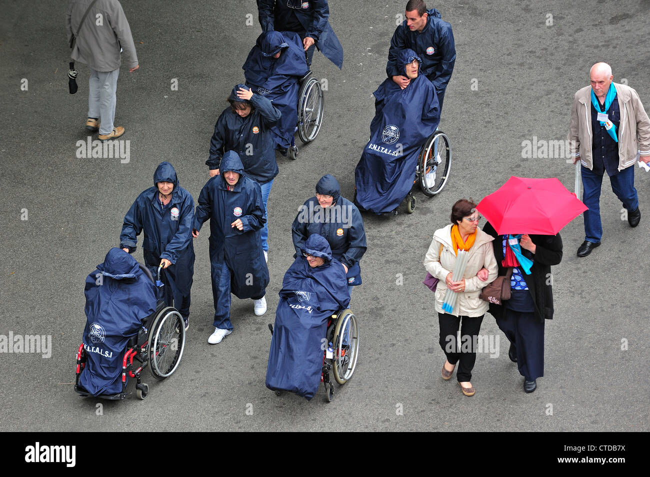 Menschen mit Behinderungen Behinderte Pilger im Rollstuhl in den regen Besuch der Wallfahrtskirche unserer lieben Frau von Lourdes, Pyrenäen, Frankreich Stockfoto