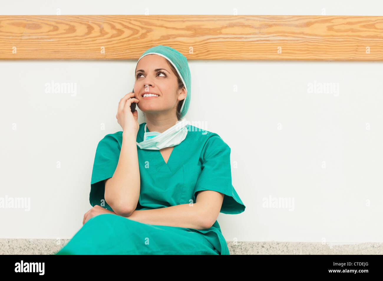 Chirurg, lächelnd, während Sie auf dem Boden sitzen und telefonieren Stockfoto