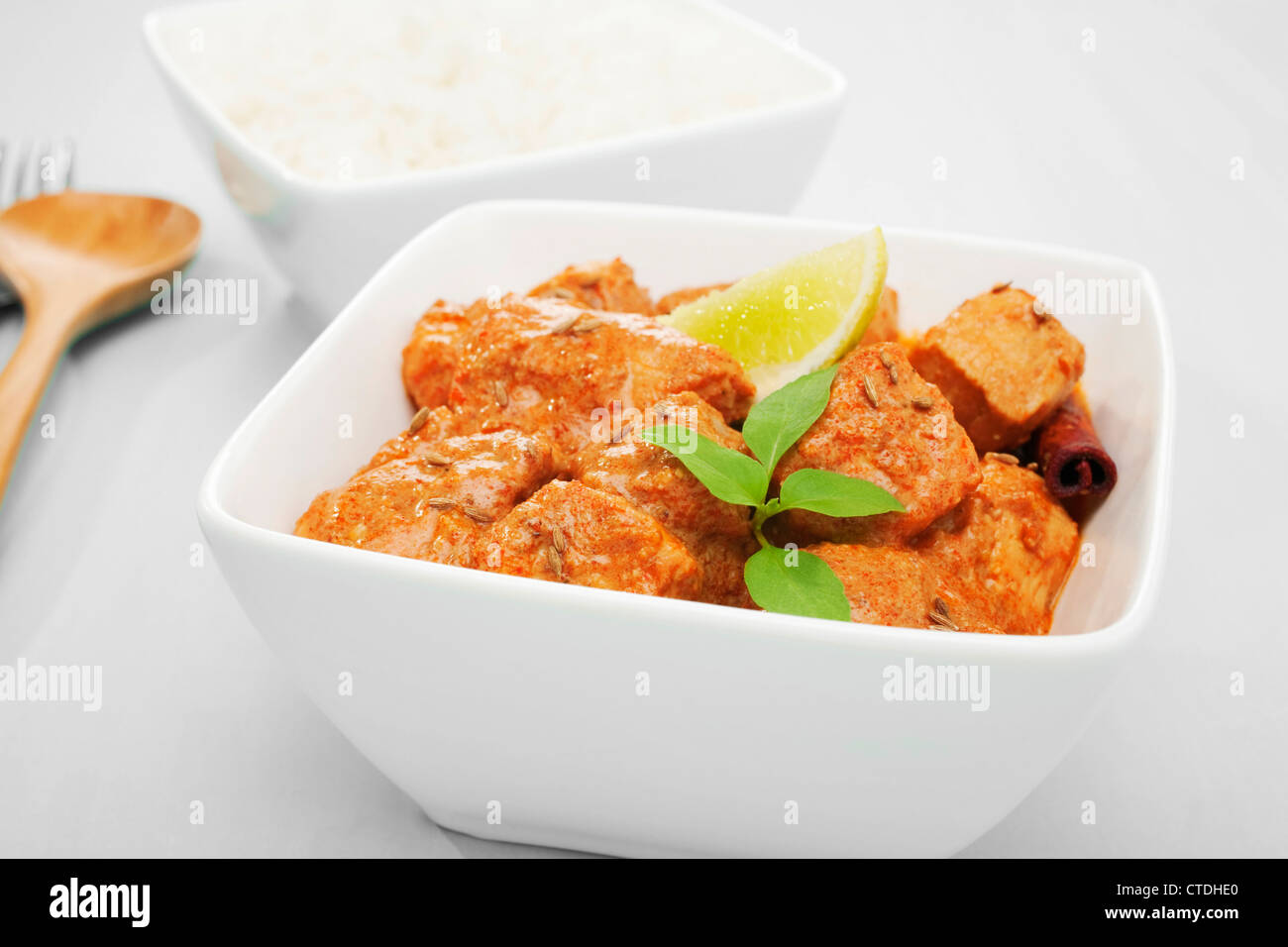 Essen indisches Curry Butter Huhn in eine quadratische weiße Schüssel auf einem blauen Hintergrund, garniert mit Limetten und thai-Basilikum. Stockfoto