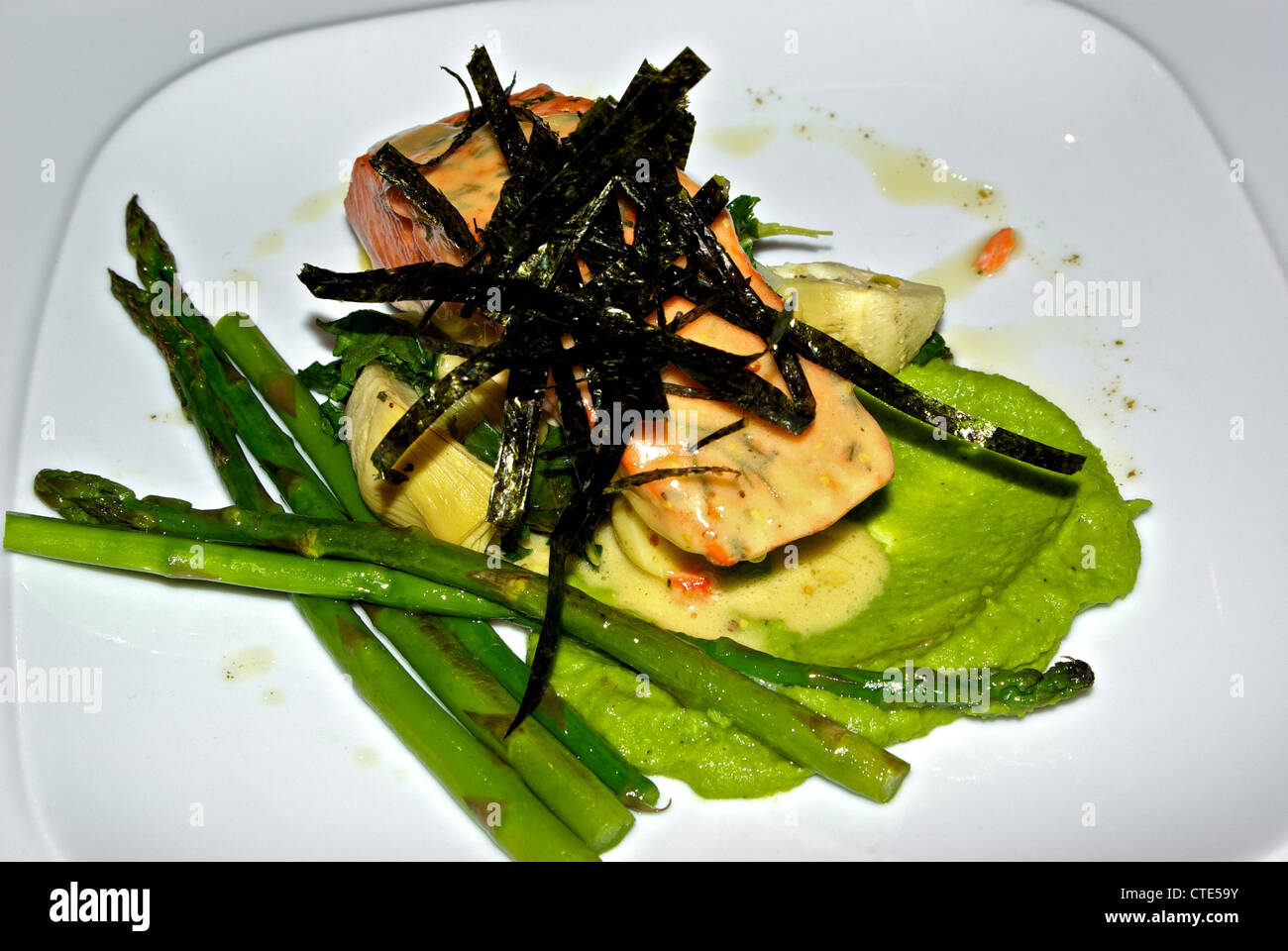 Gebackene Chinook Lachs Artischocken Spargel Spears frittierten Algen über Greenpea pürieren Zitrone Dill Sauce Meeresfrüchte Hauptgericht Stockfoto