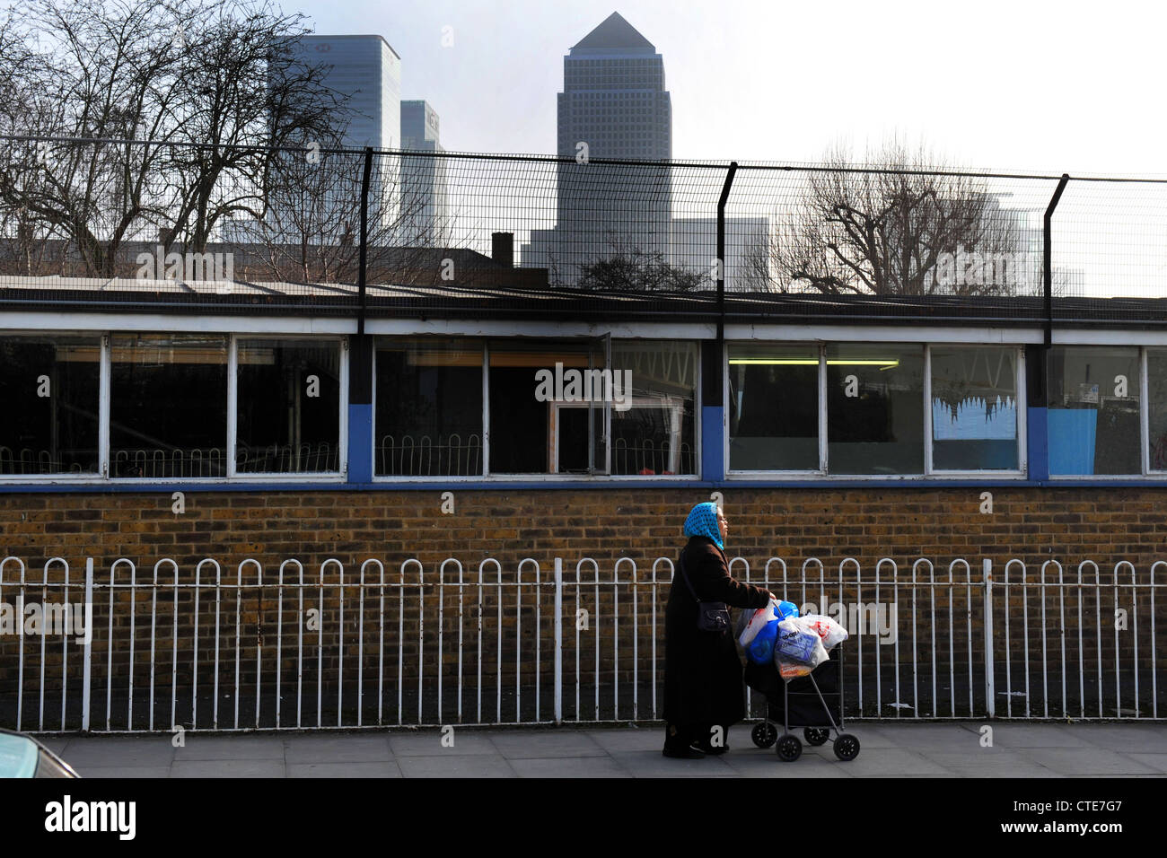 Eine Frau drückt ihre Einkaufswagen Isle of Dogs, London, im Schatten des Canary Wharf Wolkenkratzer UK Stockfoto