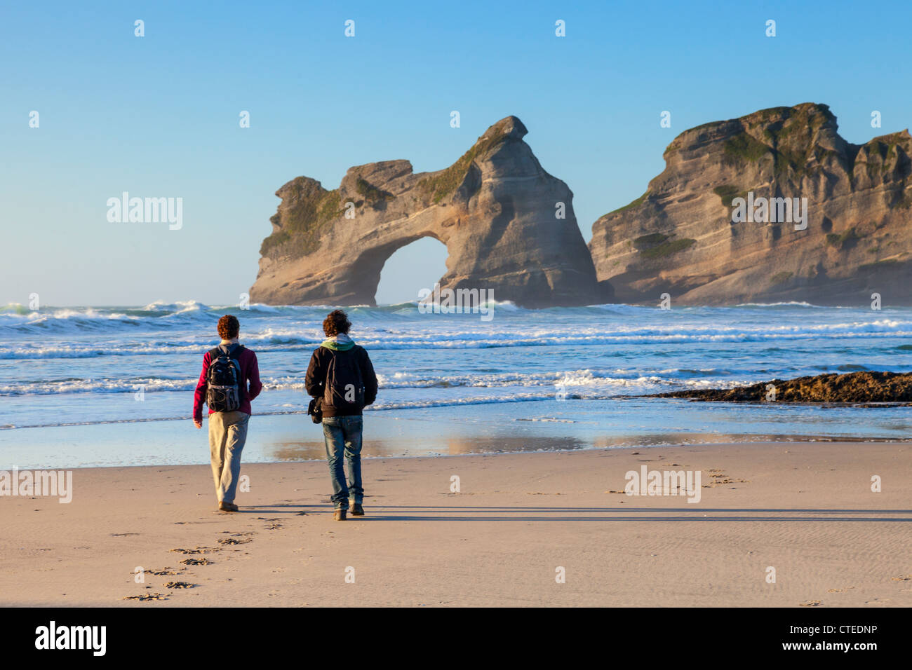 Zwei Besucher zu Fuß auf Wharariki Beach in der Region Tasman in Neuseeland in den Abend. Stockfoto