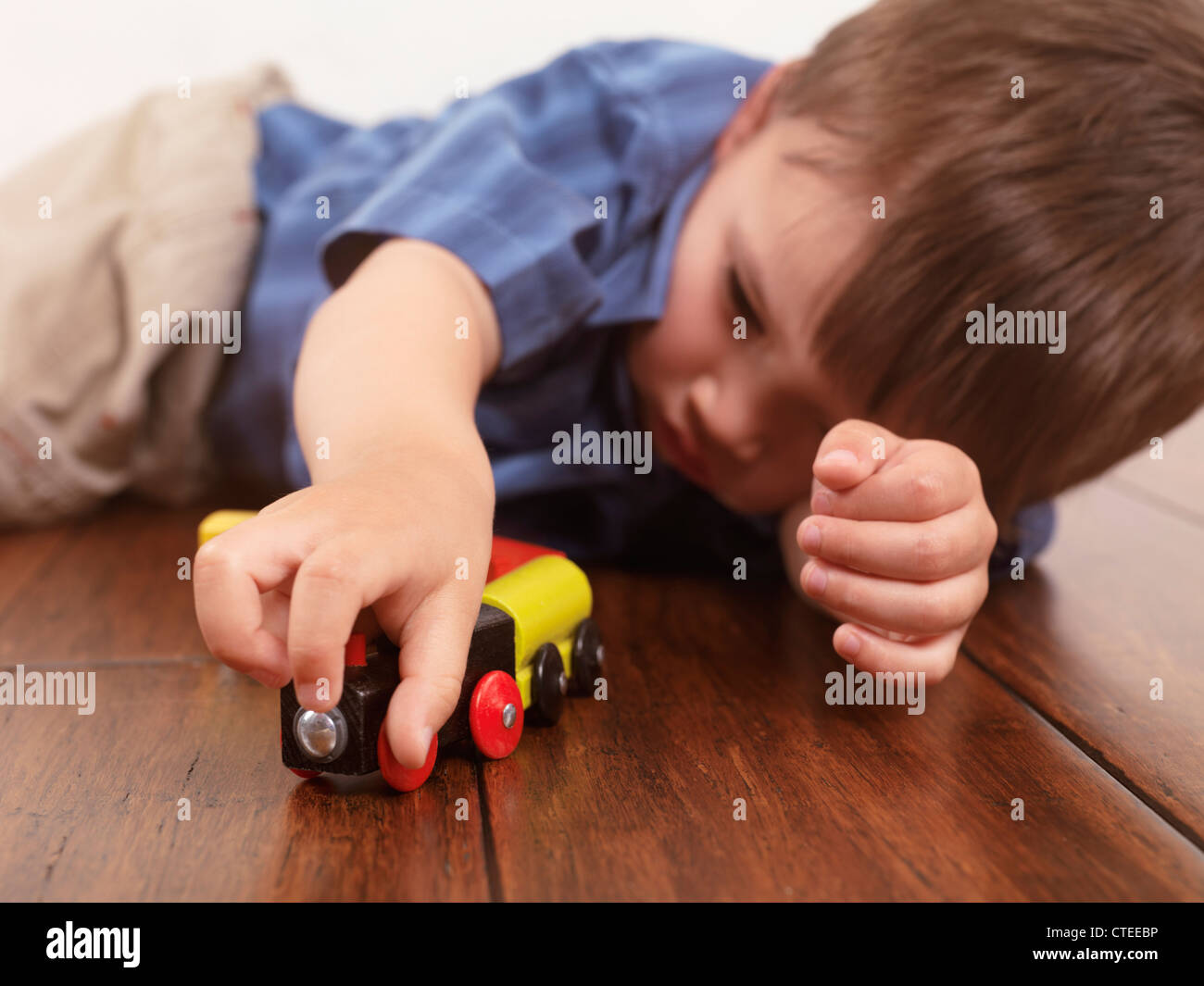 Junge spielt mit einer Spielzeugeisenbahn auf Hartholz-Fußboden liegend Stockfoto