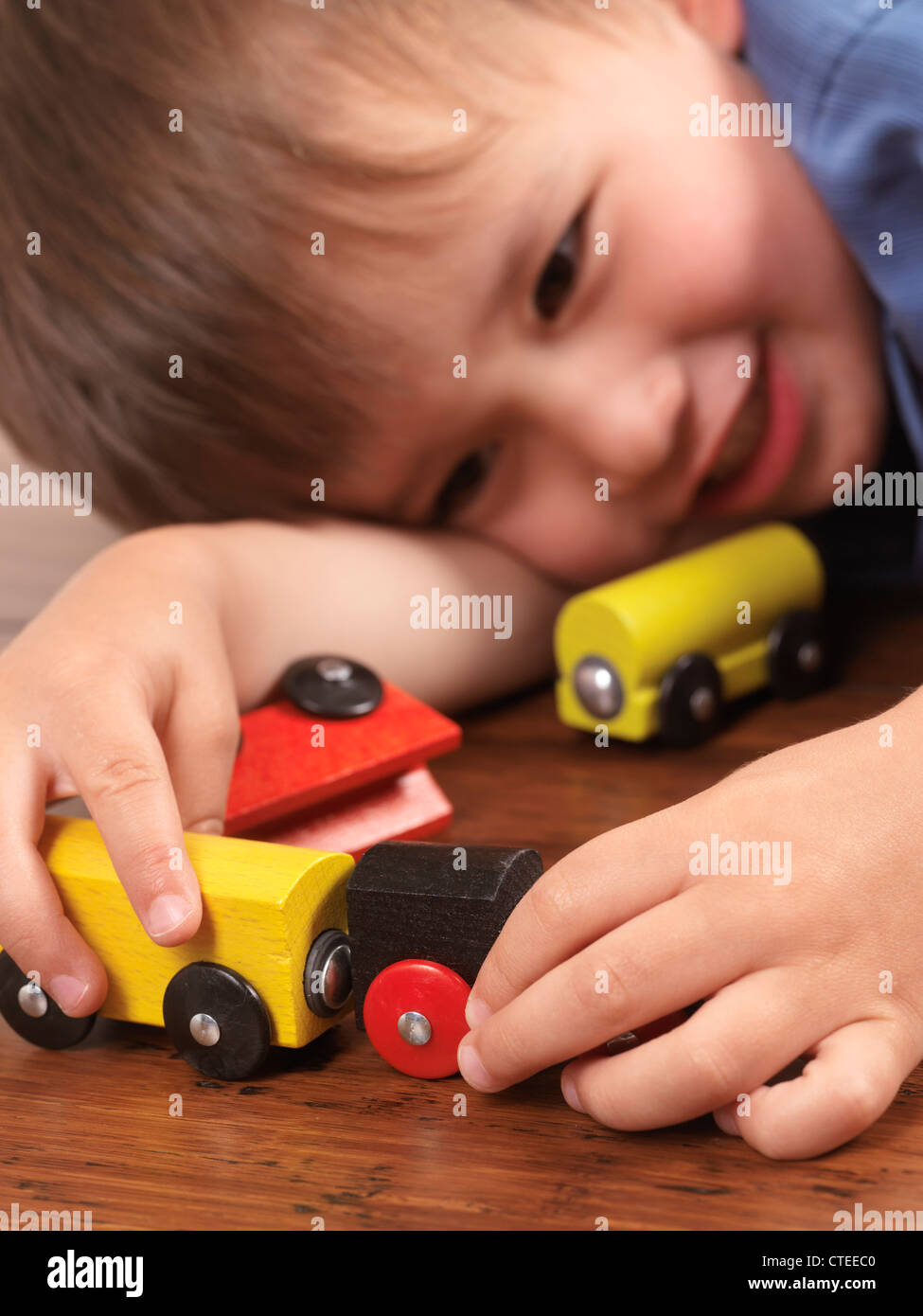 Glücklich zwei Jahre alten Jungen spielen mit einem bunten Spielzeugzug auf Parkett Stockfoto