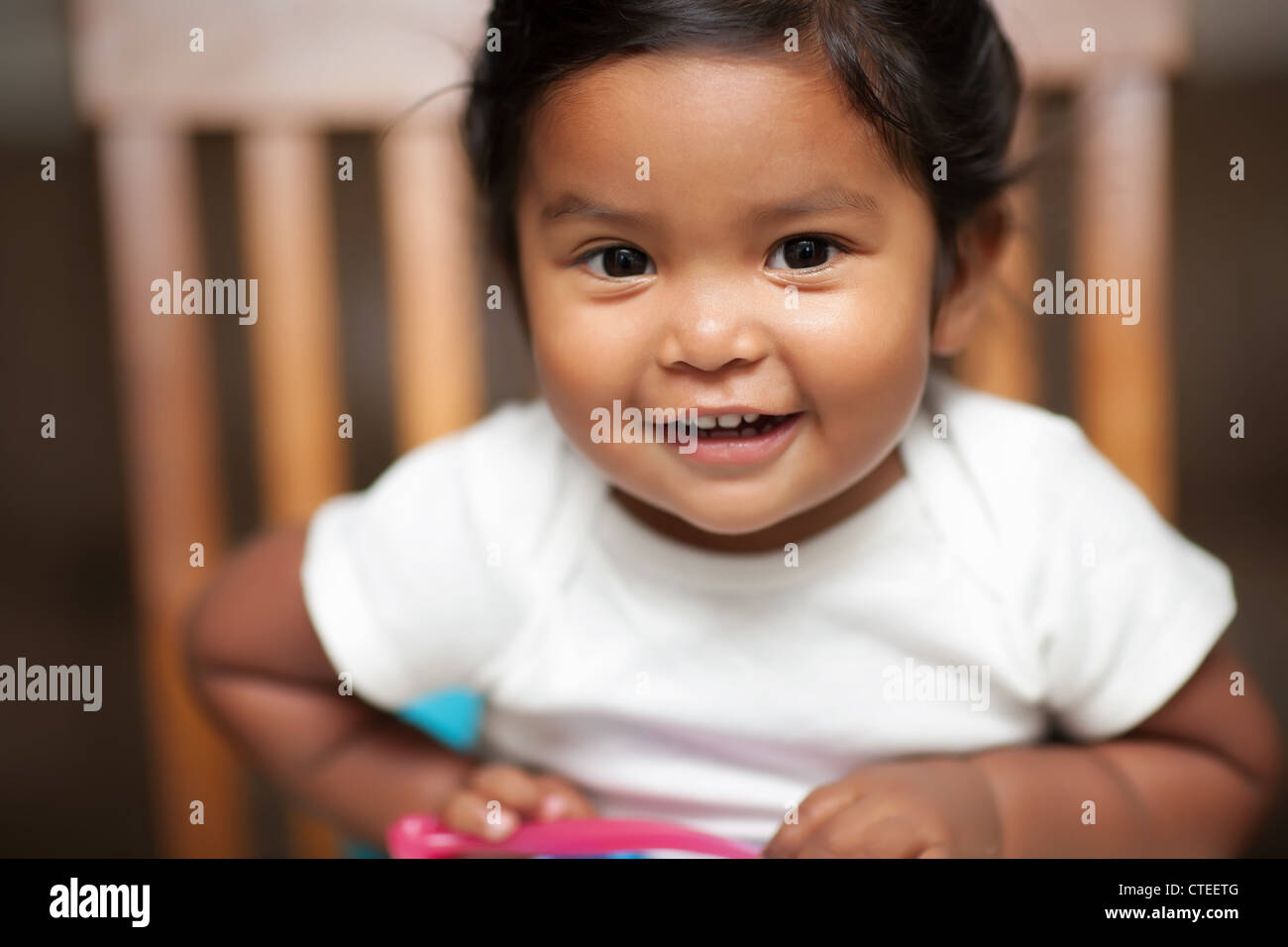 aufgeregt Babymädchen hält einen Löffel und sitzt auf einer Sitzerhöhung Stockfoto