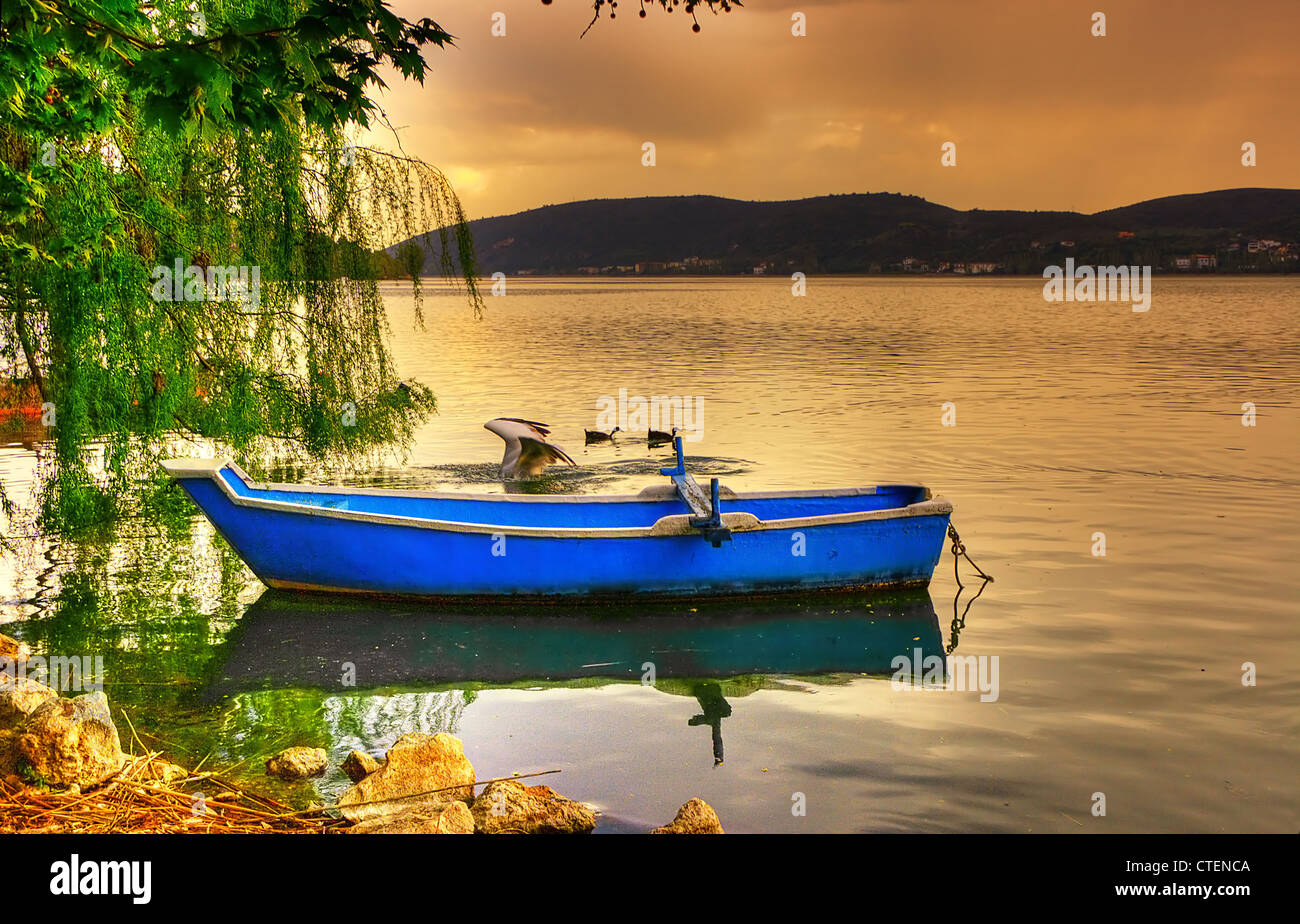 Traditionellen blauen Fischerboot in Kastoria-See mit roten bewölkter Himmel und ein Pelikan. (Makedonien, Griechenland) Stockfoto