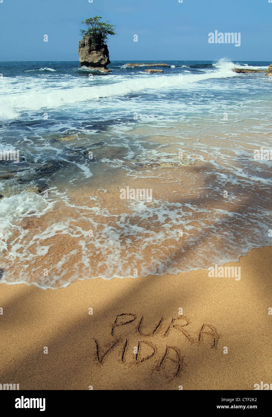 Die Worte "pura vida" in den Sand geschrieben am Meer an einem tropischen Strand mit einer felsigen Inselchen, Karibikküste von Costa Rica, Mittelamerika Stockfoto