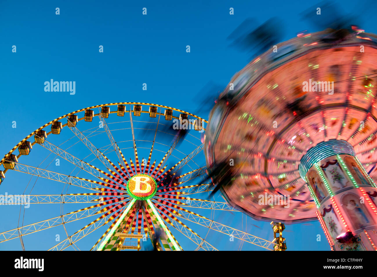 Menschen auf einer Kette Schaukel fahren in einem Vergnügungspark mit einem Riesenrad im Hintergrund, Münster. Stockfoto