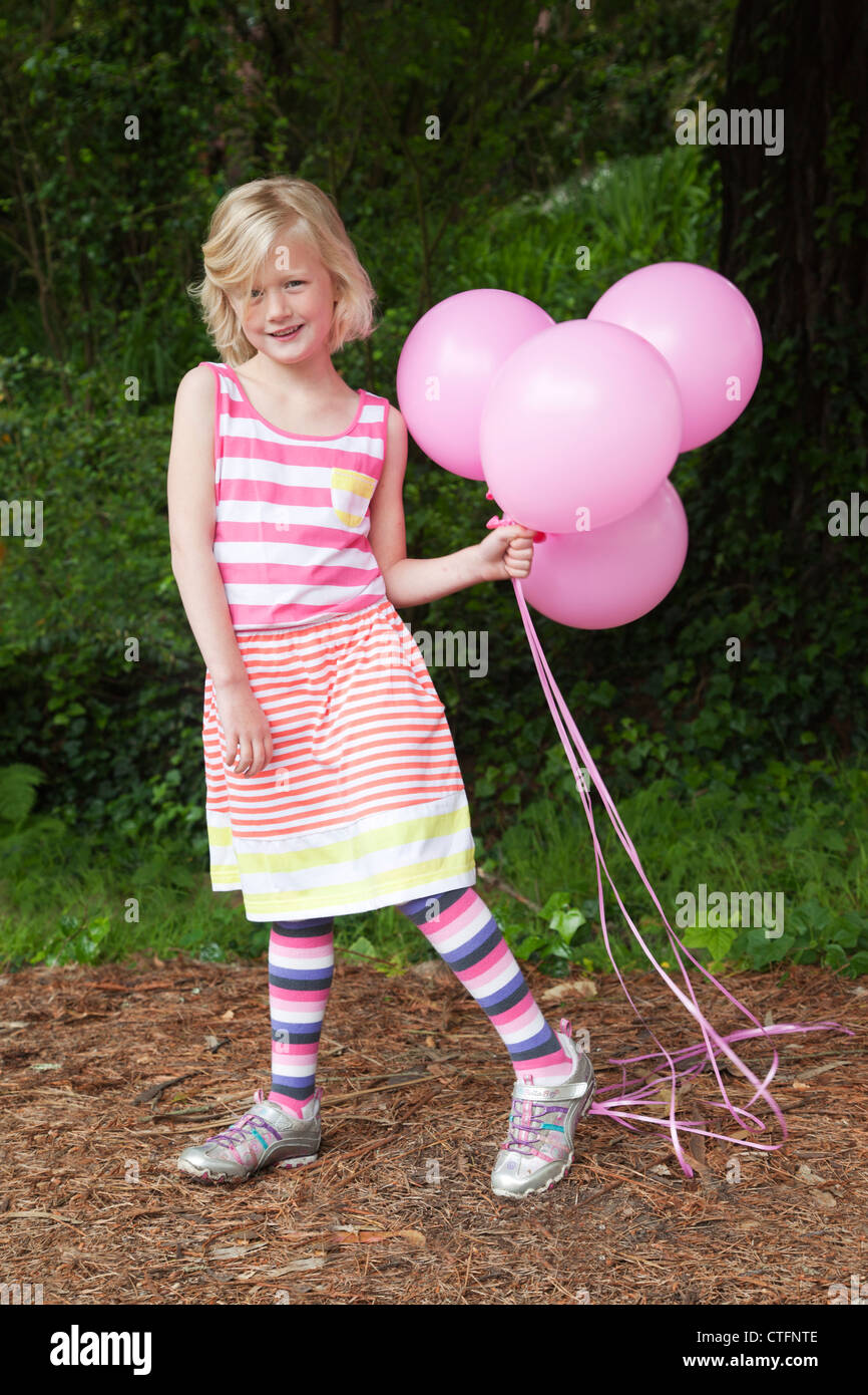 Ein kleines Mädchen im gestreiften Kleid ist rosa Ballons halten. Stockfoto