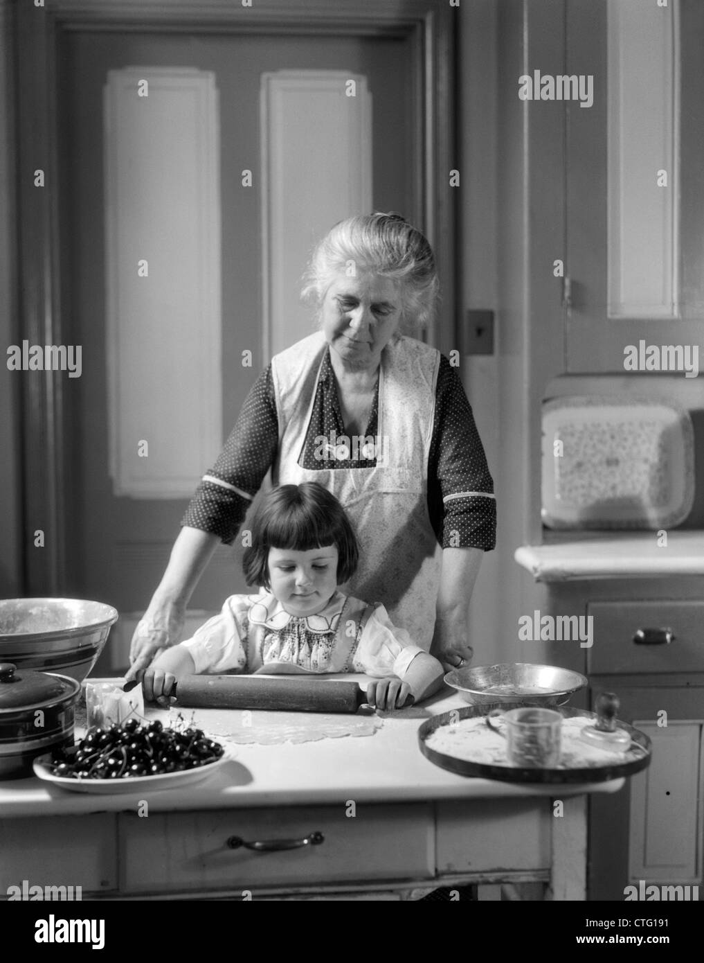 1920S 1930S GROßMUTTER BACKEN KIRSCHKUCHEN LEHRE ENKELIN UM ROLLING PIN VERWENDEN Stockfoto