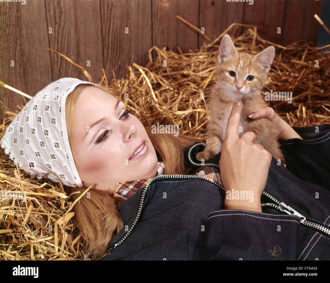 1960ER JAHRE PORTRAIT JUNGE, BLONDE FRAU LIEGEND SCHEUNE STROH HEU ROT TABBY KITTEN HAUSTIER HALTEN Stockfoto