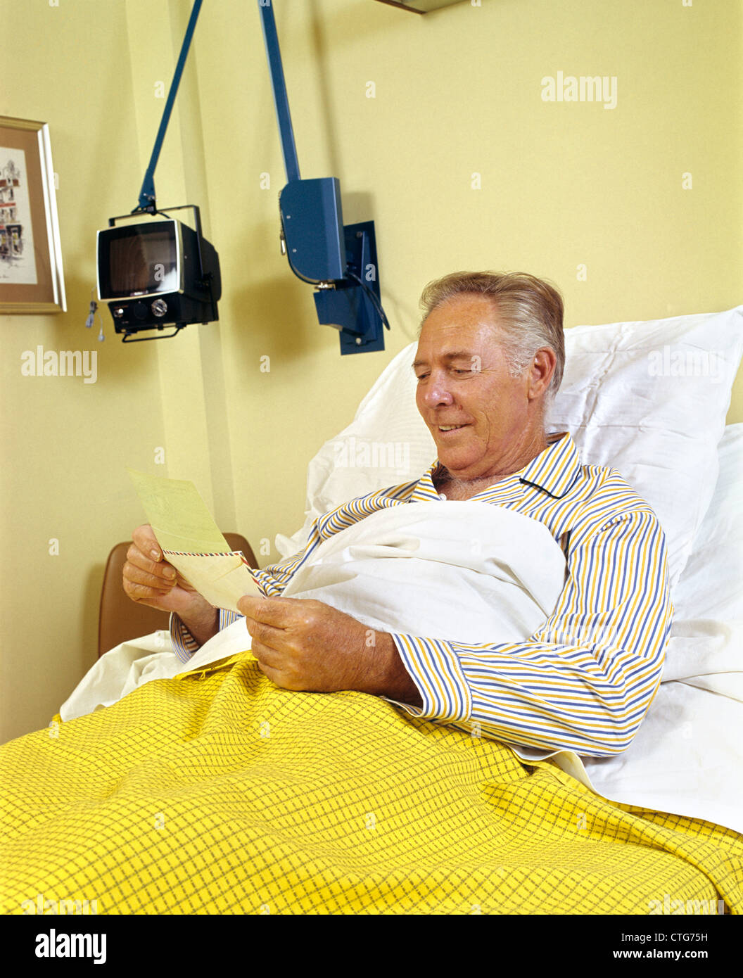 1980ER JAHREN LÄCHELND SENIOR MANN IM KRANKENHAUS BETT ERÖFFNUNG POST BLICK AUF VERSICHERUNG CHECK Stockfoto