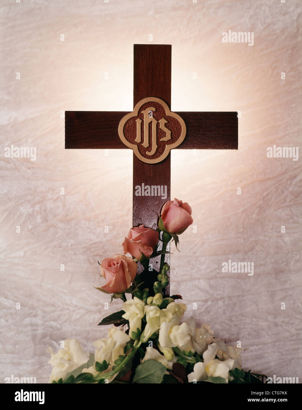HOLZKREUZ MIT BUCHSTABEN IHS UND WEIßEN SNAPDRAGON BLUMEN UND ROSA ROSEN AN DER BASIS Stockfoto