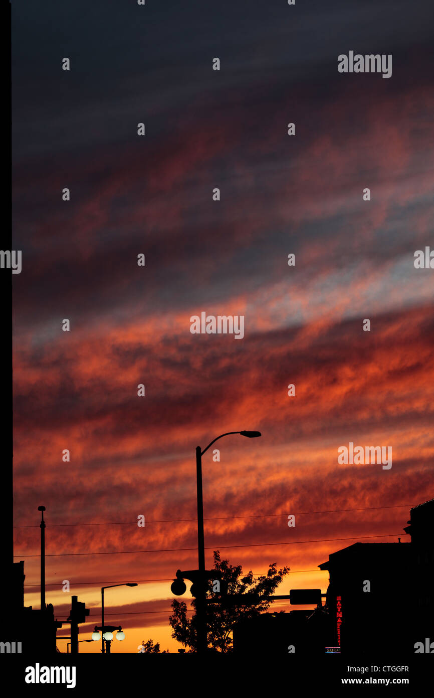 Lebhaft rot und orange Sonnenuntergang, umrahmt von Lichtmasten und Fassaden Stockfoto