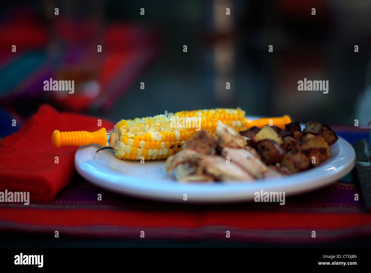 Teilweise gegessen Mais Maiskolben auf einem roten Gedeck blaue Platte und Huhn mit Kartoffeln. Stockfoto