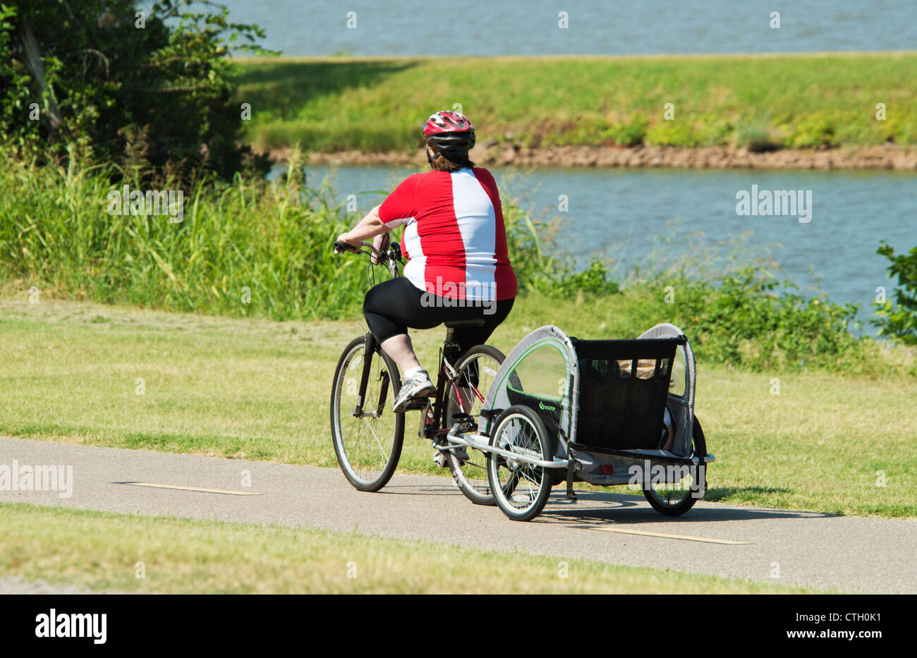 Eine beleibte Frau, ziehen einen Kiddy-Karren fährt ihr Fahrrad auf Spuren von einem See in Oklahoma, USA. Stockfoto