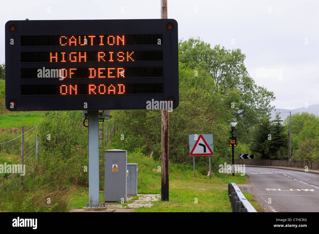 Matrix-Schild an A85 Warnung "nehmen Vorsicht hohes Risiko der Hirsche unterwegs" mit langsamen vor der Kurve und hohen Zaun Crianlarich Scotland UK Stockfoto