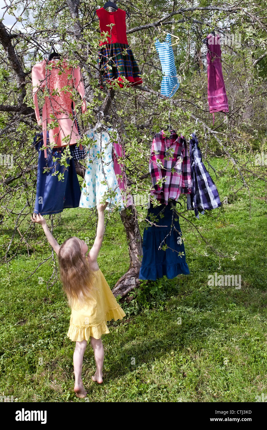 kleines Mädchen mit Kleidern, die Zweige hängen vor den Baum stehen Stockfoto
