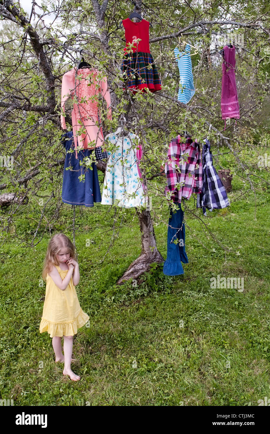kleines Mädchen mit Kleidern, die Zweige hängen vor den Baum stehen Stockfoto
