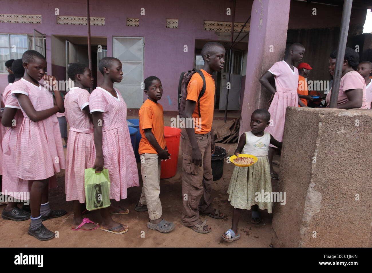 Schülerinnen und Schüler Line-up für ihr Mittagessen bei der NGO finanziert gehütet Kinder Grundschule in den Kosovo Slumviertel von Kampala Stadt Stockfoto