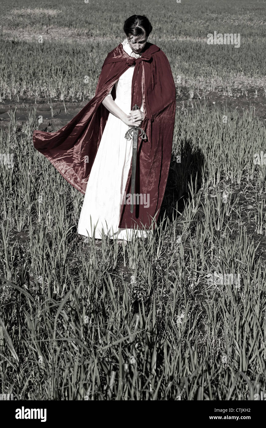 eine Frau in einem roten Umhang in einem Feld mit einem Schwert Stockfoto