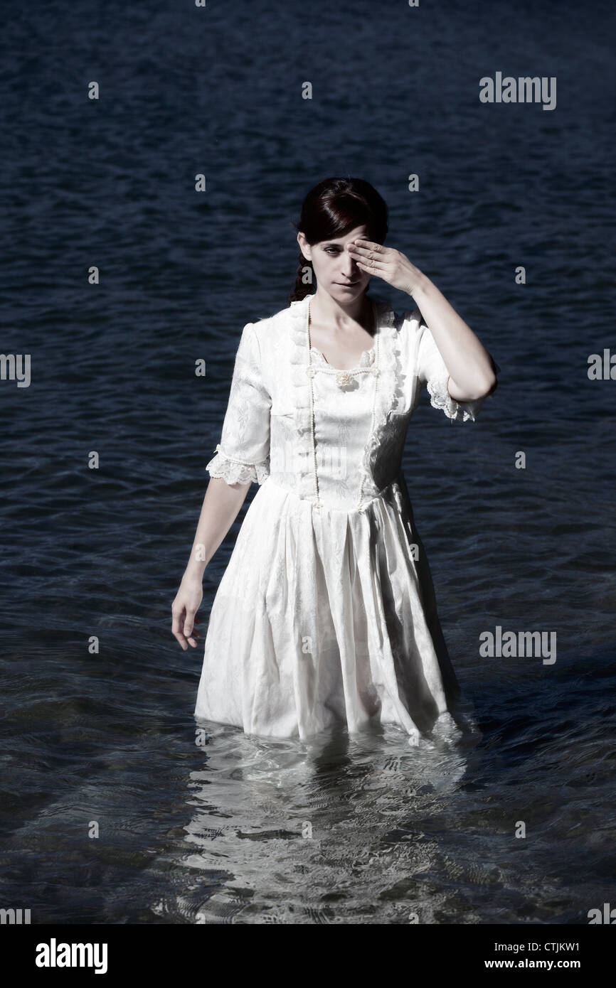 eine Frau in einem weißen viktorianischen Kleid im Wasser stehn und hält ein Auge auf Stockfoto