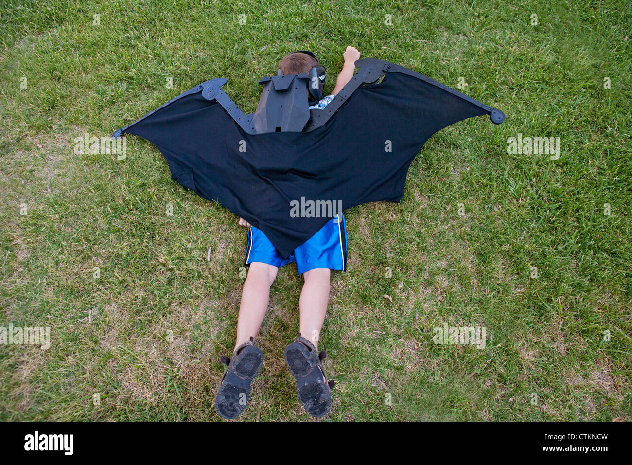 Junge vorgibt, Batman, tragen riesige Flügel zu sein vorgibt zu fliegen, während im Gras. Stockfoto