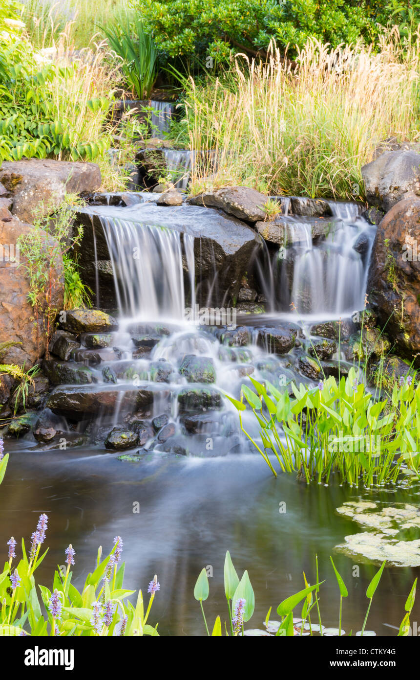 Einen fließenden Wasserfall mit Rasen und Blumen im park Stockfoto