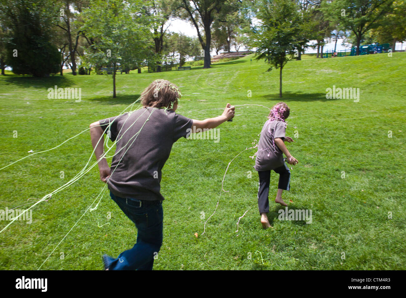 13 Jahre alter Junge jagt jüngerer Bruder mit einer Dose Silly String spray - Latex String in einem Park. Stockfoto