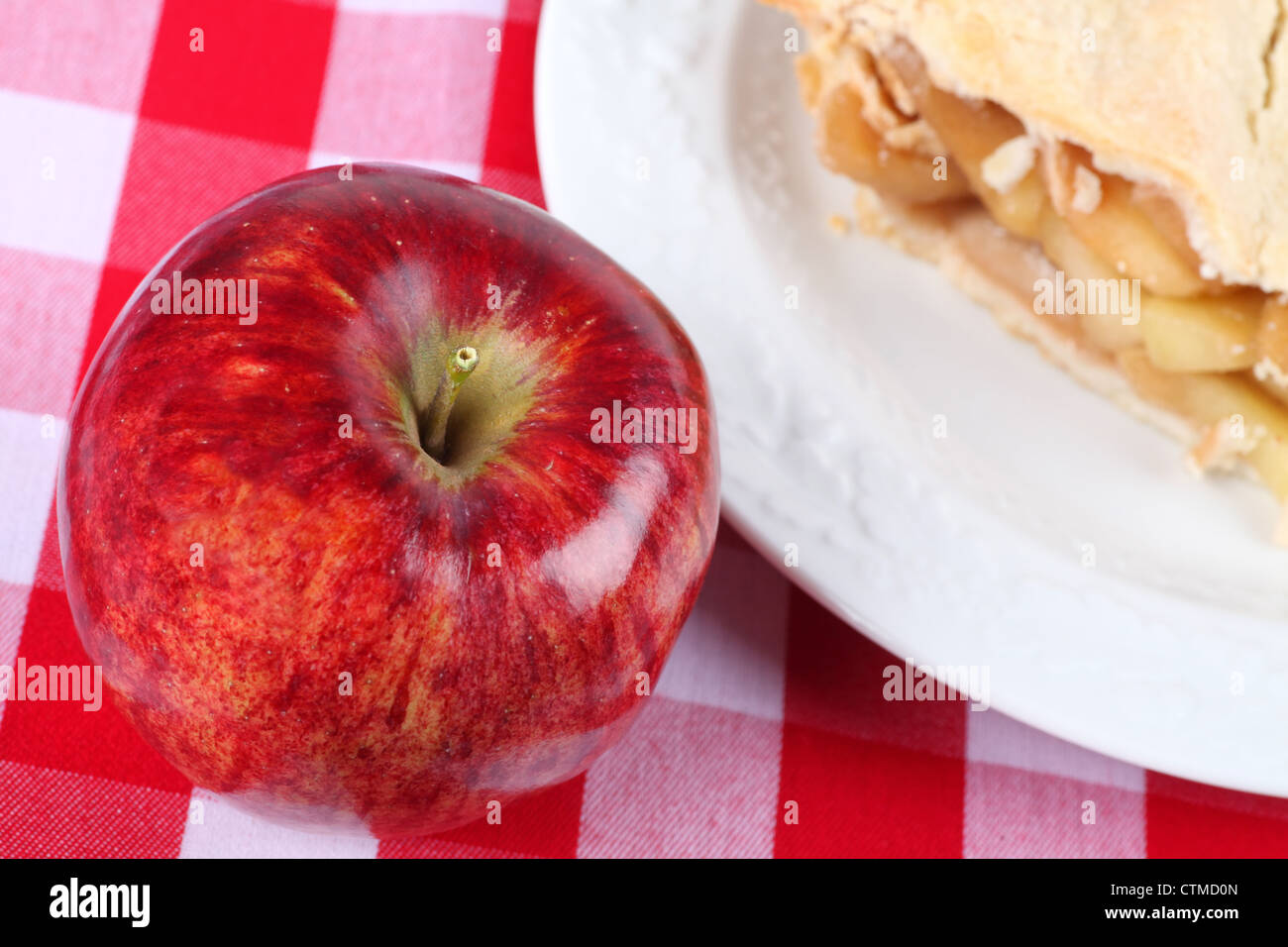 Ein reifer roter Apfel auf karierte Tischdecke neben einem Stück Apfelkuchen. Stockfoto