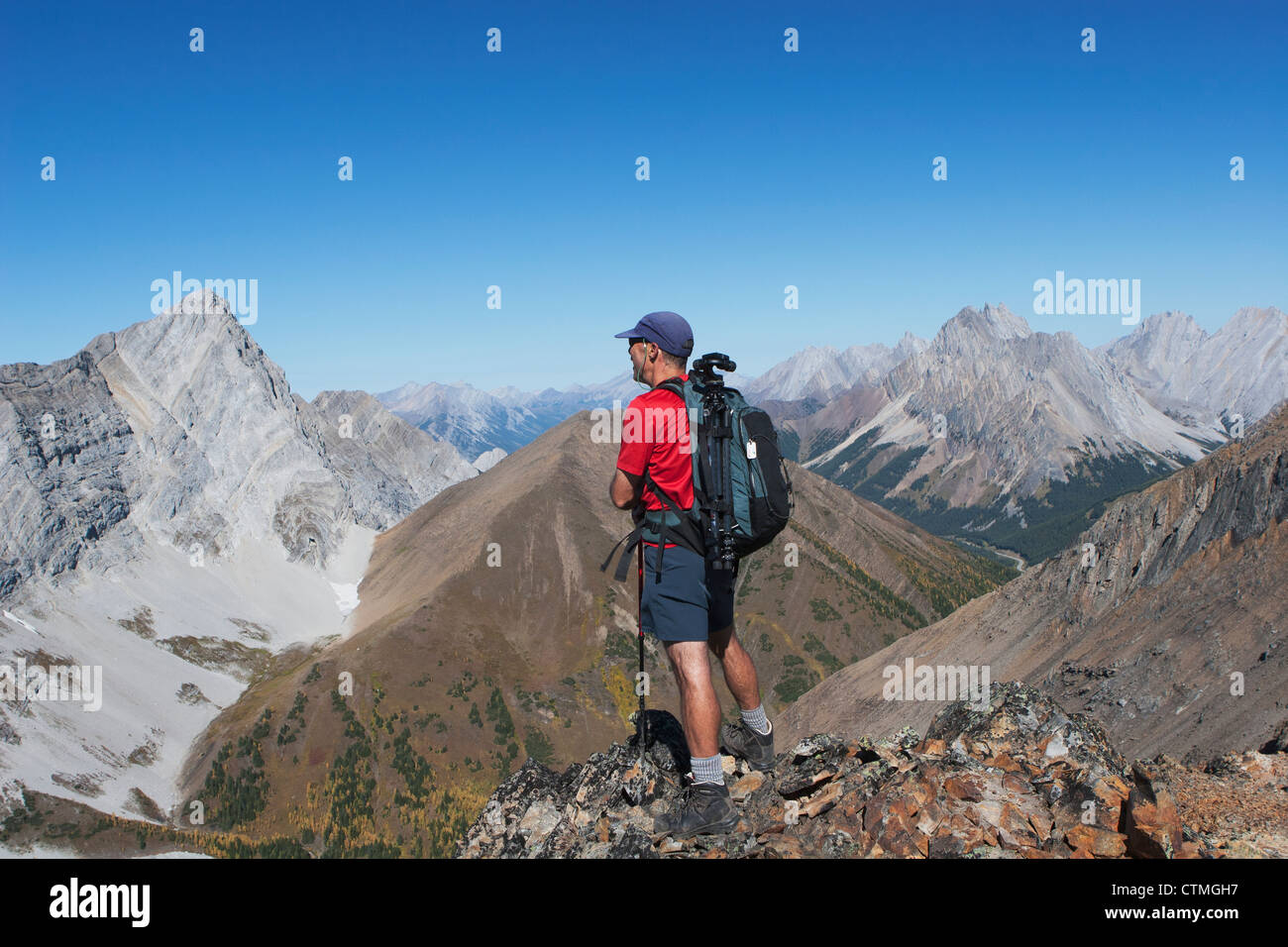 Männliche Wanderer auf Bergrücken mit Blick auf Tal und Berge In der Ferne mit blauem Himmel; Alberta, Kanada Stockfoto