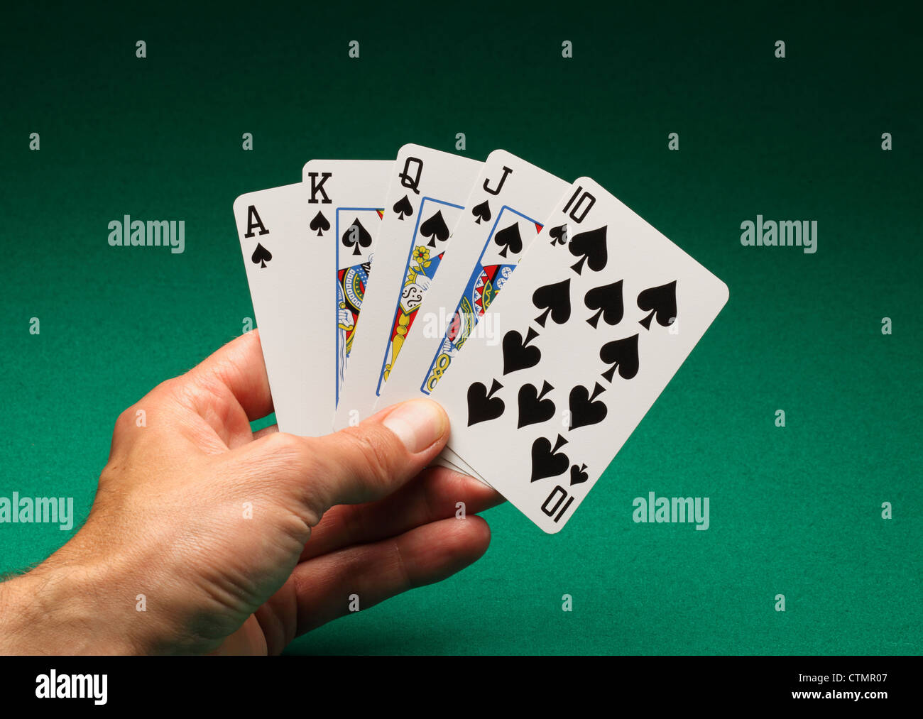 Eines Mannes Hand mit Spielkarten am grünen Tisch. Ein Royal Flush Pik in das Spiel von Poker Stockfoto