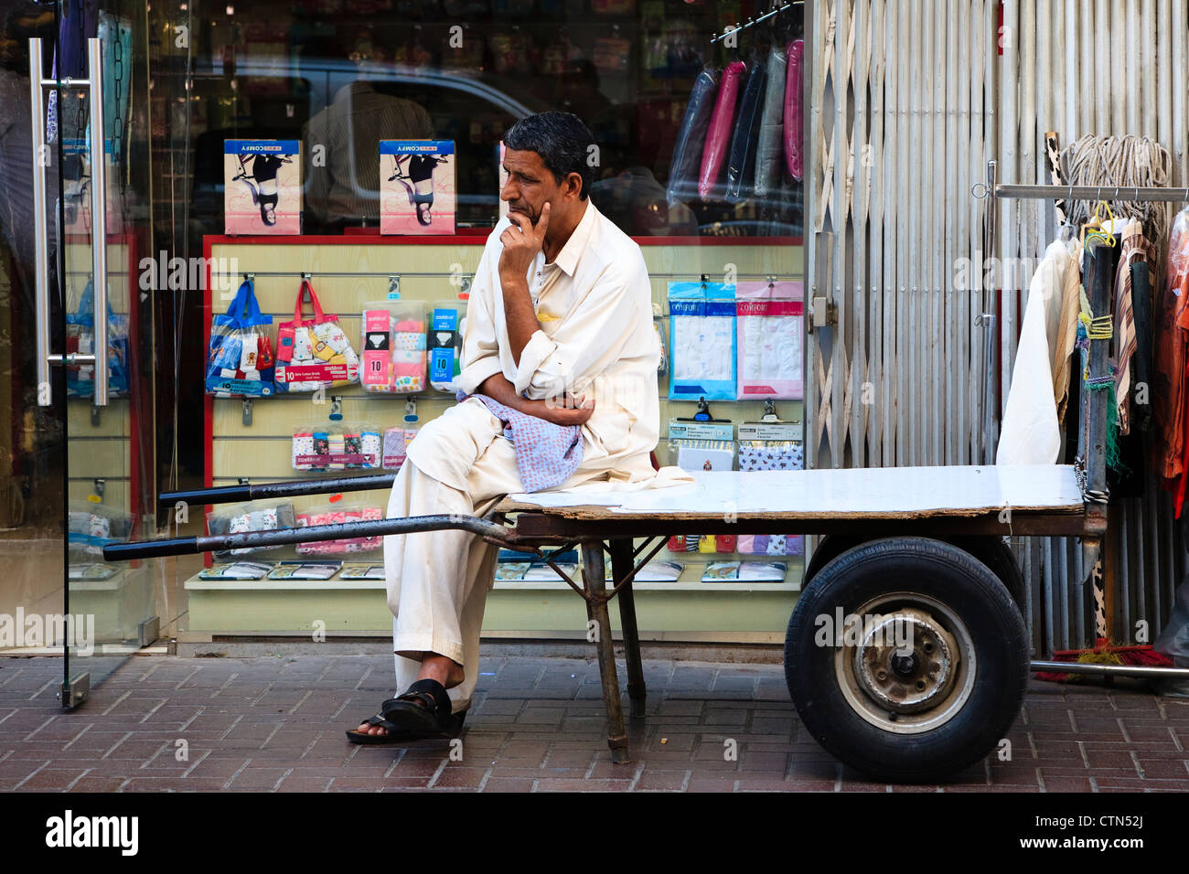 Arabische Mann sitzt auf seiner Schubkarre außerhalb einen Shop, alte Stadt Souk, Dubai. Stockfoto