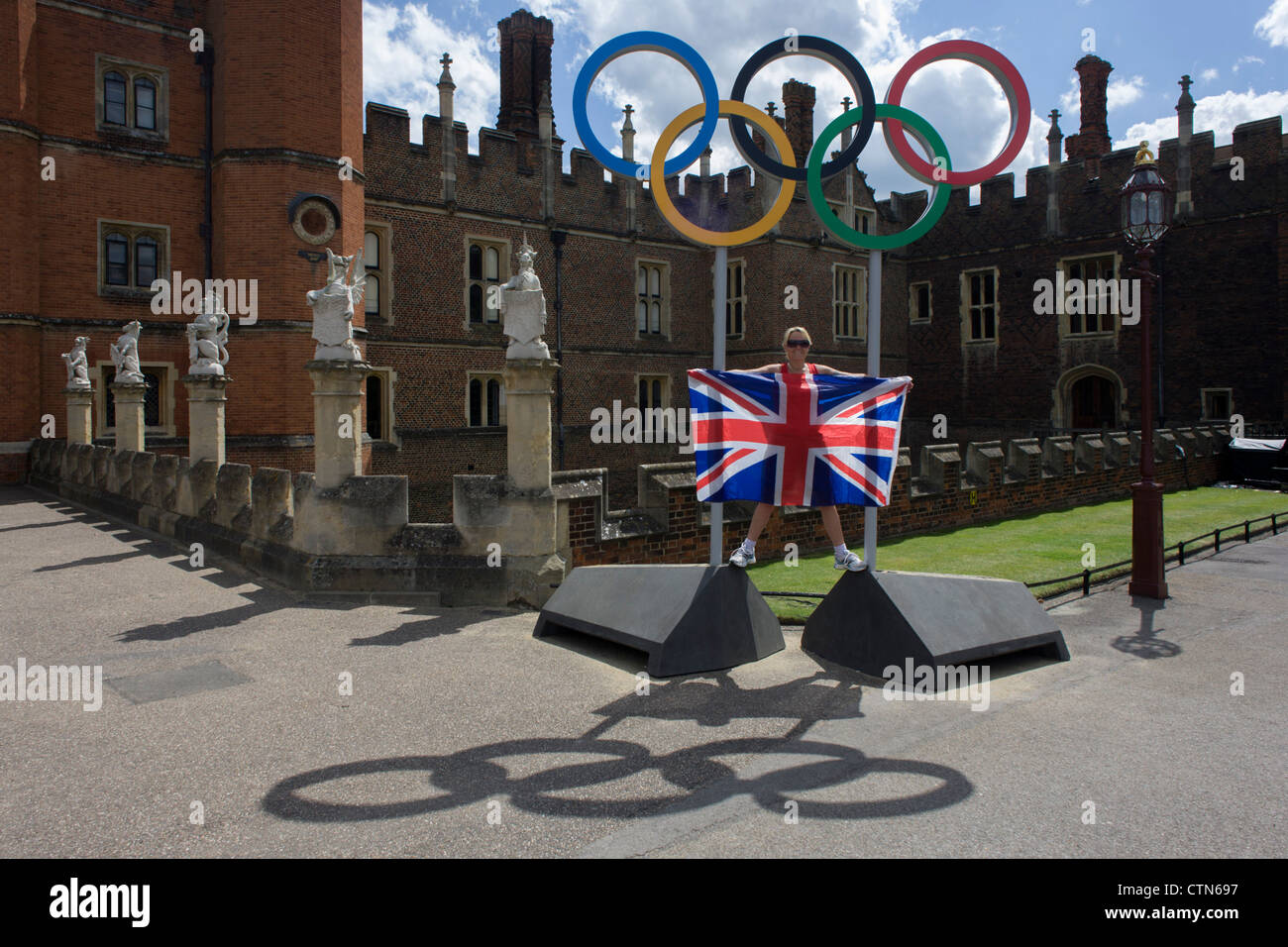 London-Lady steht für ein Erinnerungsfoto auf die Olympischen Ringe, die am Eingang des König Heinrich der achtes Hampton Court Palace am ersten Tag des Wettbewerbs der Straßenrennen der Olympischen Spiele London 2012 250 km Mens stehen. Ausgehend vom Zentrum von London und berühmten Wahrzeichen der Hauptstadt vor der Überschrift heraus in ländlichen England an den zermürbenden Box Hill in der Grafschaft Surrey. Lokalen Südwest Londoner säumten die Strecke, in der Hoffnung auf britische Favorit Mark Cavendish gewinnt Team GB erste Medaille aber schließlich enttäuscht wenn Kasachstans Alexandre Vinokourov schließlich Gold gewann. Stockfoto