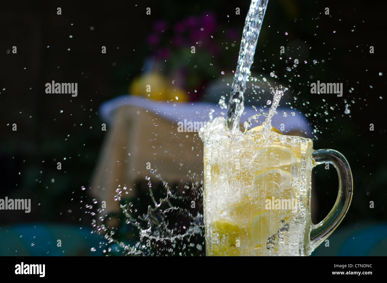 Gießen Sie Wasser und Splahing in Glaskrug voller Zitronen an sonnigen Tag. Stockfoto