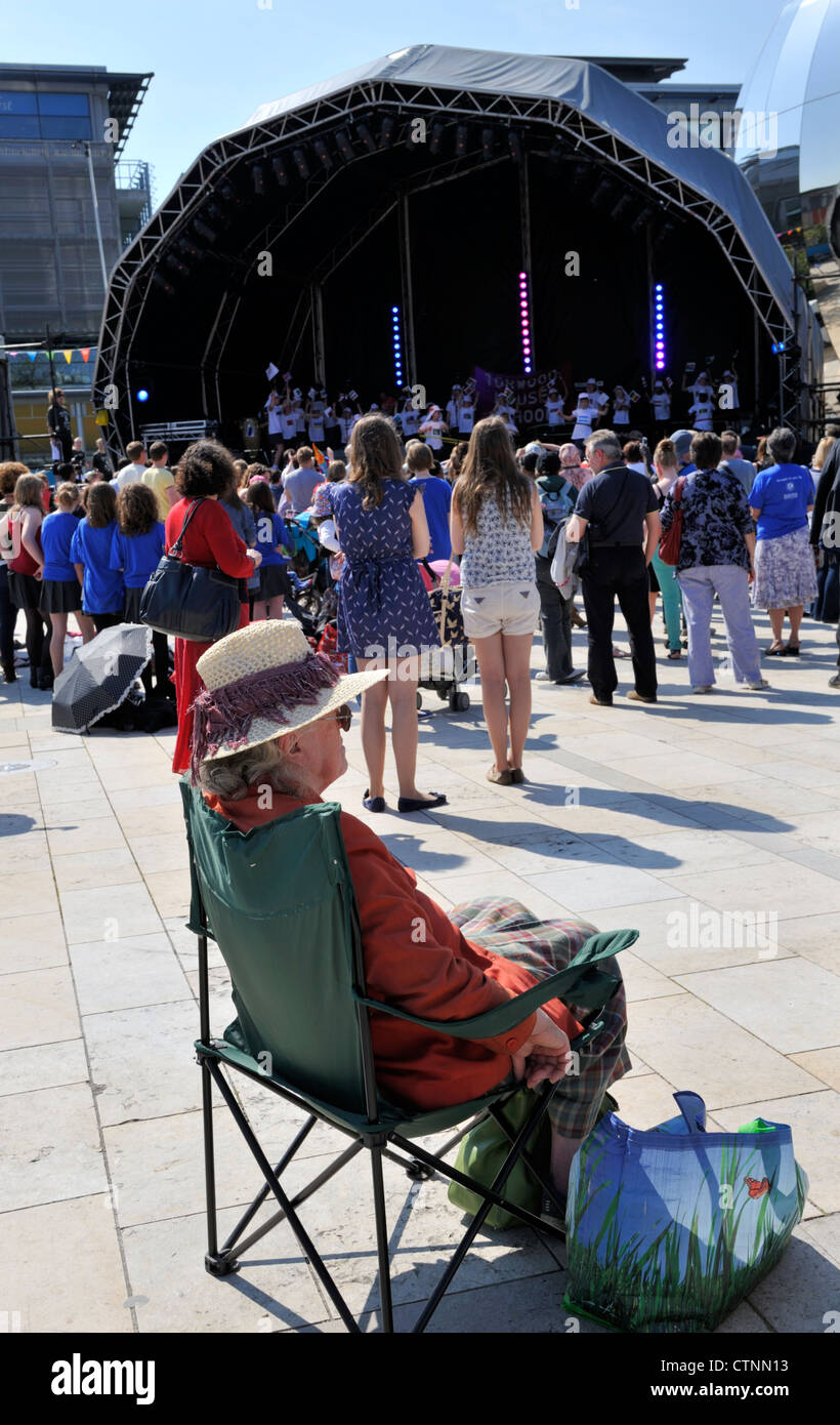 Publikum beobachten open Air Konzert am Bristol Millennium Square mit älteren Frau sitzen auf Stuhl Stockfoto
