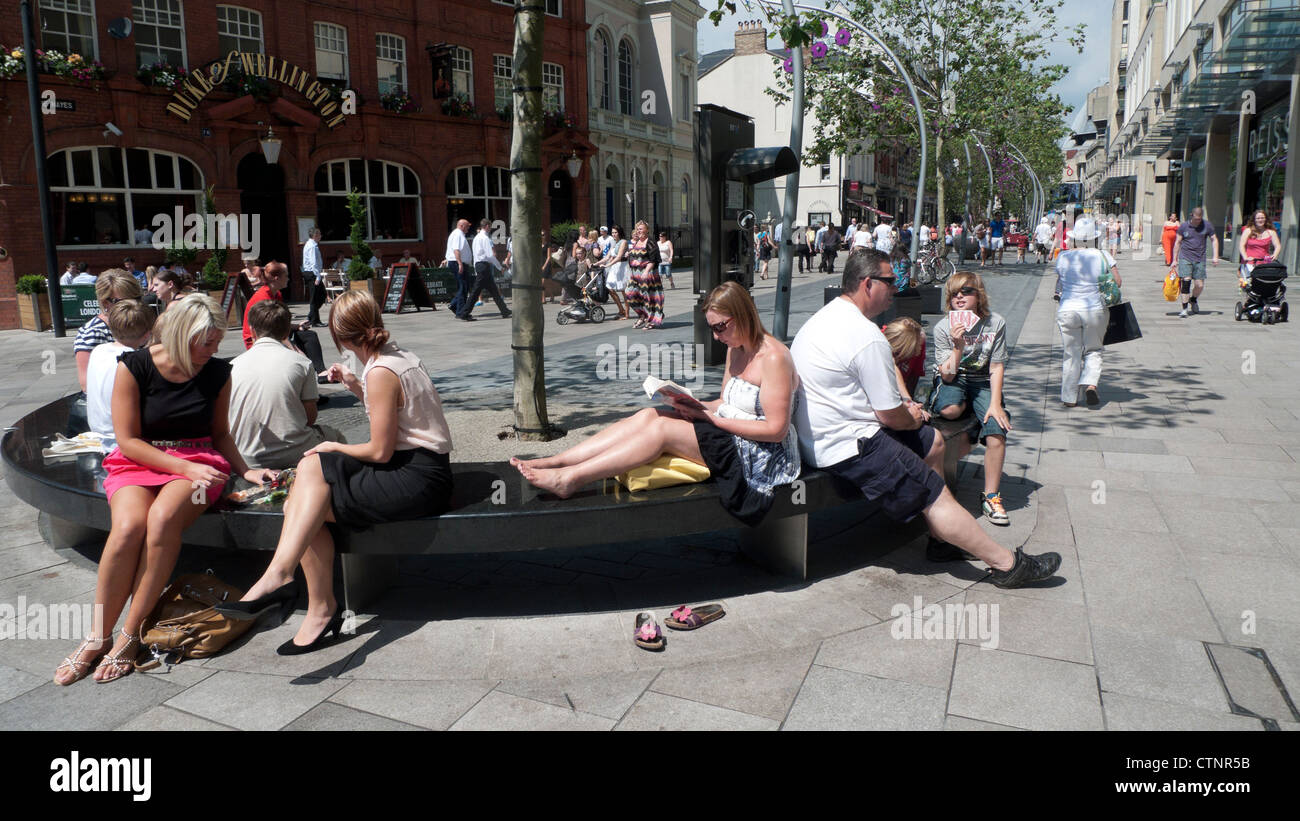 Menschen entspannen sich auf Bänken Frau lesen in Cardiff City Centre Fußgängerzone Einkaufsstraße im heißen Sommersonnenschein Wales UK KATHY DEWITT Stockfoto