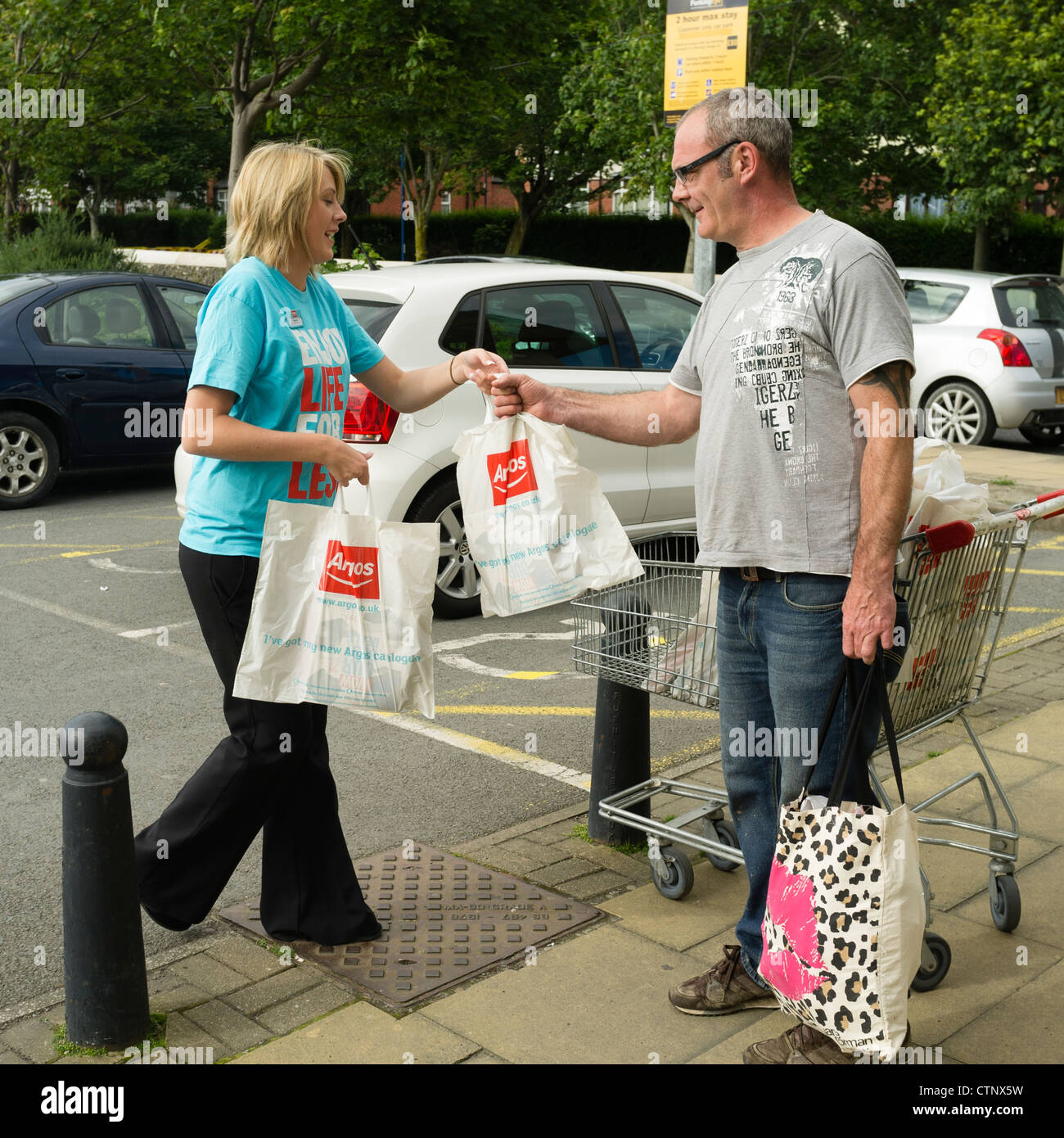 Eine Frau Verkäuferin austeilen Plastiktüten mit Argos Store Kataloge UK Stockfoto