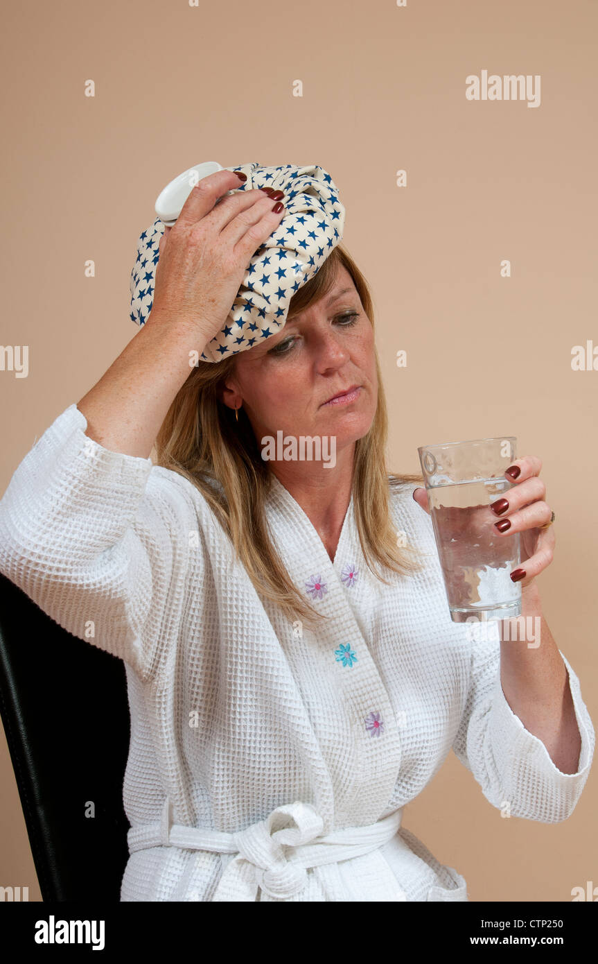 Frau mit Eisbeutel am Kopf leiden einen Kater und ein Glas Wasser zu trinken Stockfoto