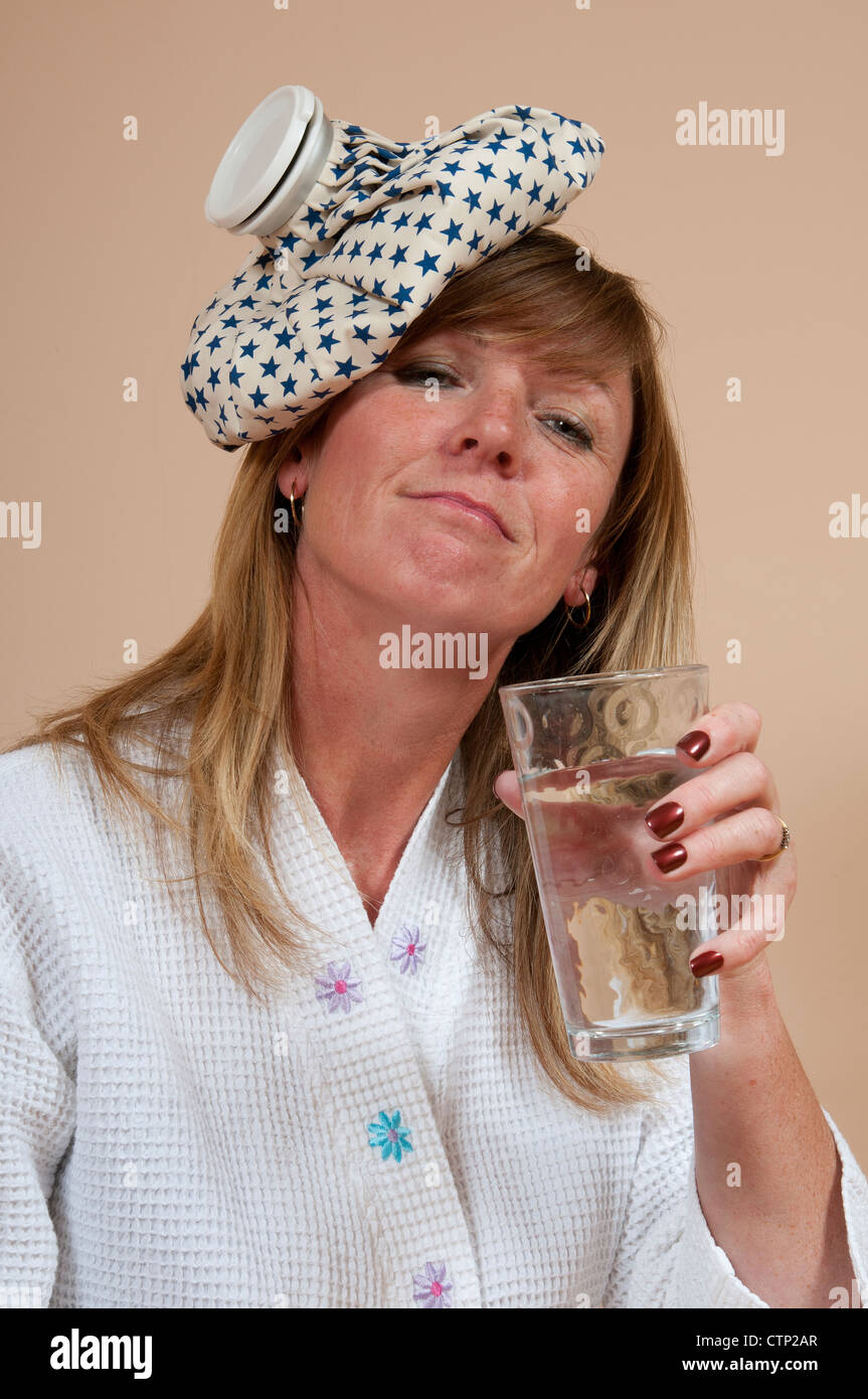 Frau mit Eisbeutel am Kopf leiden einen Kater und ein Glas Wasser zu trinken Stockfoto