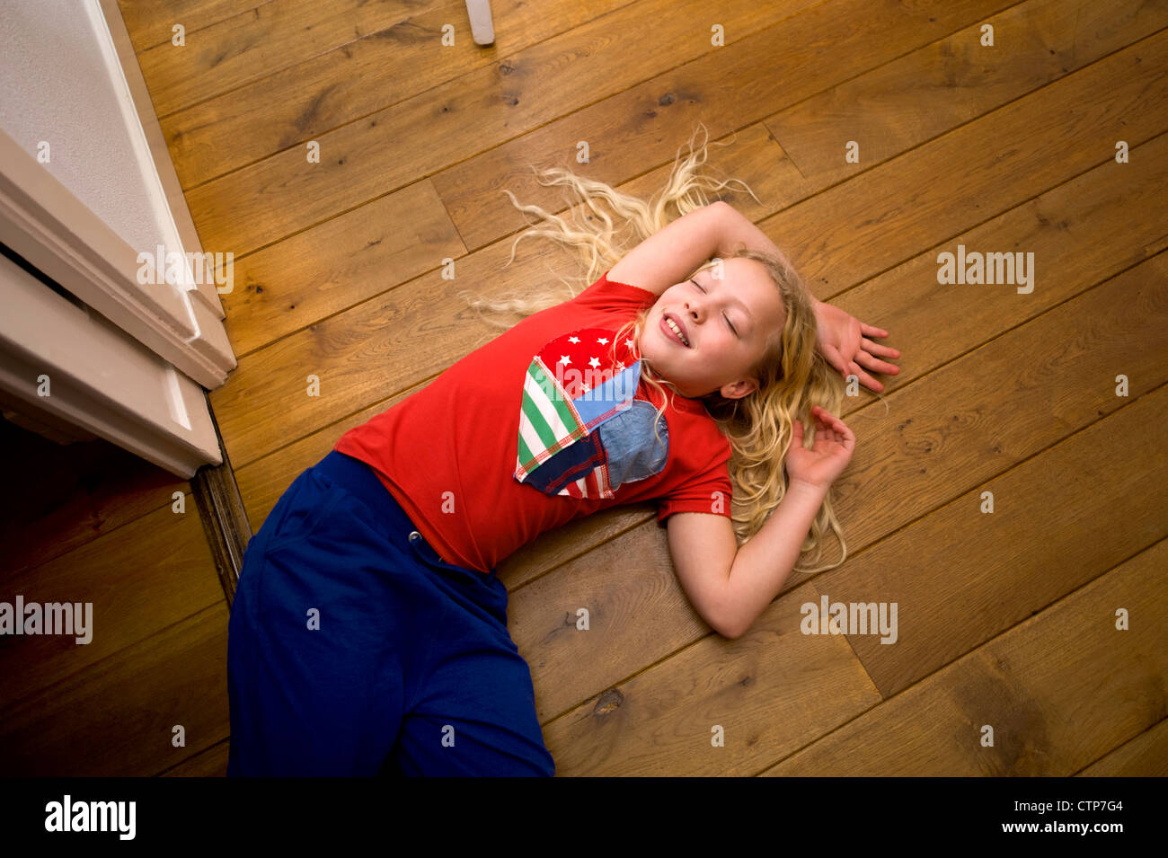 Kleines blondes Mädchen vorgibt, schlafen auf dem Boden ihres Hauses Stockfoto