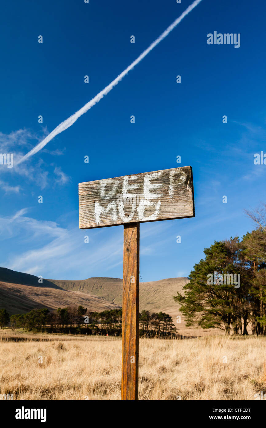 Ein handgemaltes Schild an einem Holzstab Warnung Menschen in tiefen Schlamm an einem See in einem Nationalpark in Wales.  Ein Jet Trail oben. Stockfoto