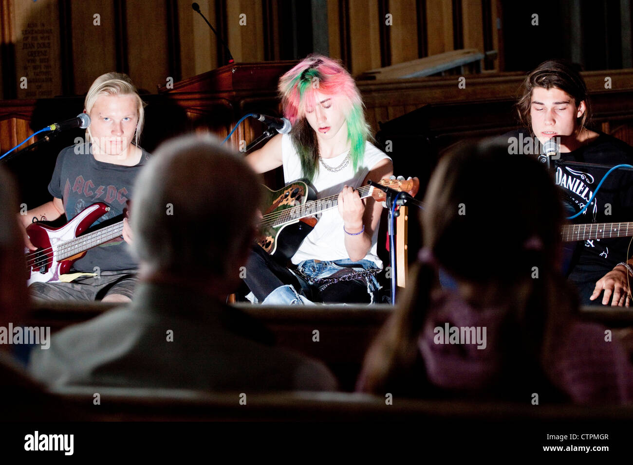 Sitzen drei junge Rock-Gitarristen spielen zu sitzendem Publikum Stockfoto