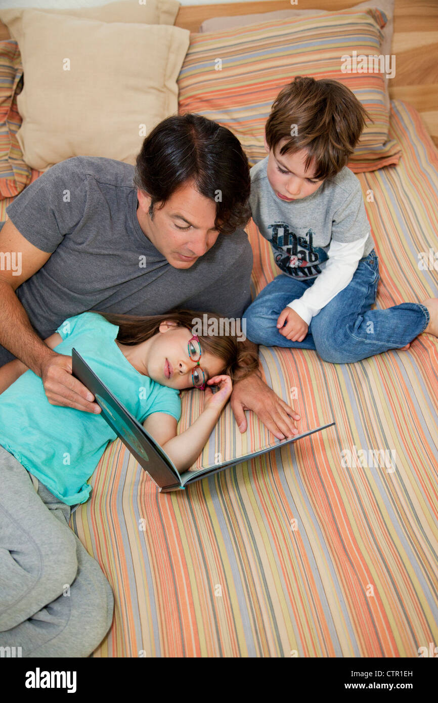 Vater, Tochter und Sohn liegen auf dem Bett ein Buch zu lesen. Stockfoto