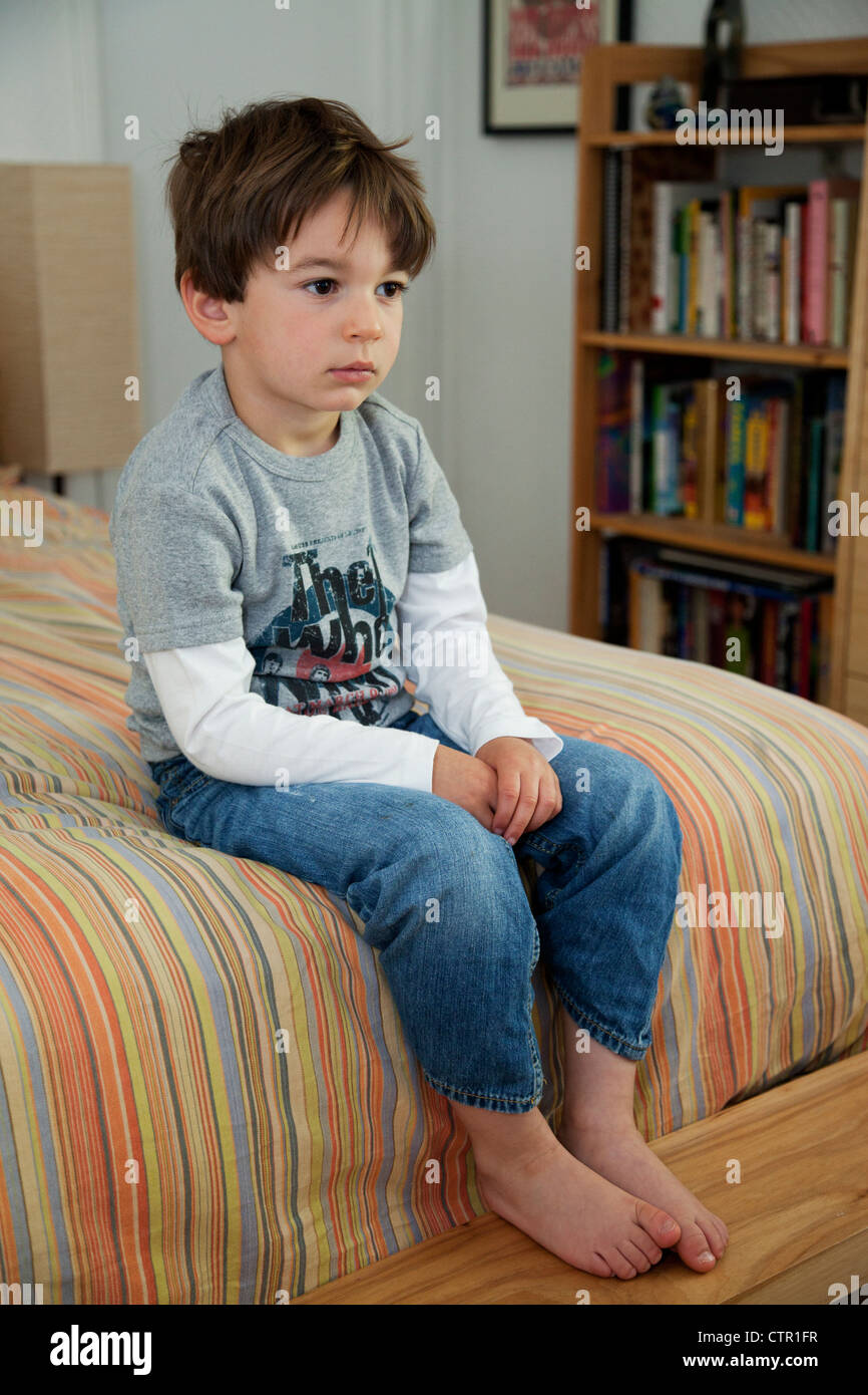 Ein drei Jahre alter Junge sitzt auf einem Bett. Stockfoto